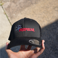 Black cap with red text held by a hand on a concrete surface