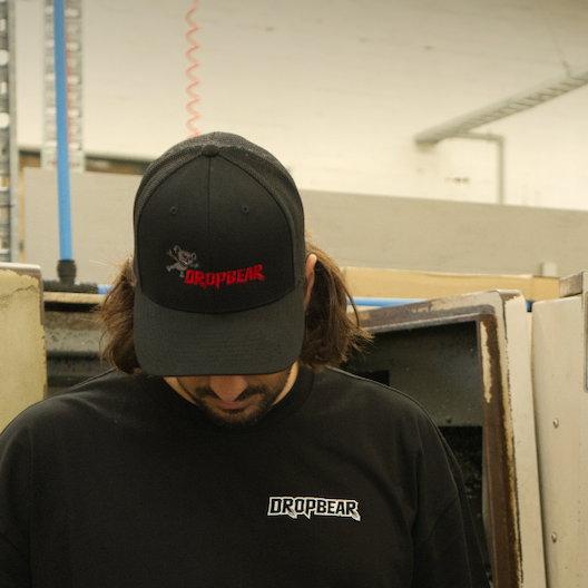 Person wearing a black cap and black t-shirt with 'DROPBEAR' logo in an industrial setting